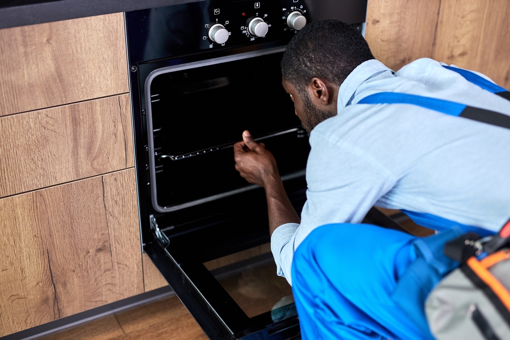 African,Handyman,Examining,Electric,Oven,In,Kitchen,At,Home.,Appliance